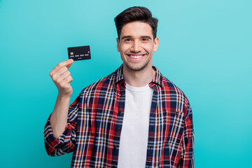 Photo of cute cheerful man dressed plaid shirt smiling rising bank card isolated turquoise blue...