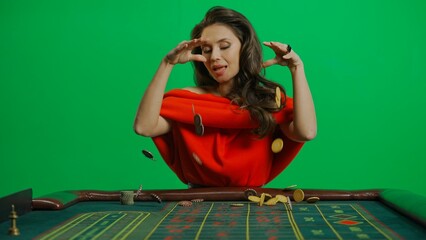 Gorgeous female in studio on chroma key green screen. Appealing woman in red dress at the roulette table dropping many chips on the table.