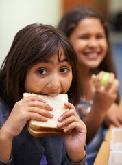 Hungry girl, portrait and student eating sandwich in classroom at school for meal, break or snack...