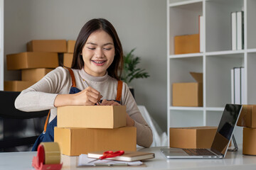SME entrepreneur small business online sales concept, happy Asian business owner working on computer and boxes at home, SME Procurement parcel delivery box sending to customer,