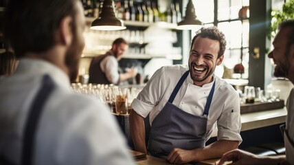 Cheerful male bartender in apron laughing with customers at a trendy bar.