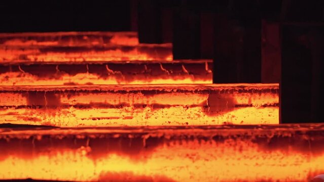 Metallurgy factory. Steel production in the workshop. Hot metal sheet slides along the conveyor. Heavy industry. Red hot steel metal billets after molten steel casting. Hot steel bars on the conveyor.