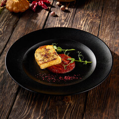 Pan-fried cheese with berry sauce, served on a black plate with a rustic wooden background