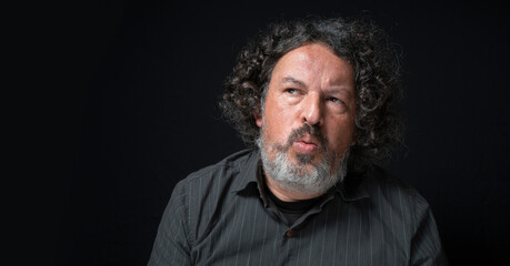 Man with white beard and black curly hair with cautious expression, looking left suspiciously,...