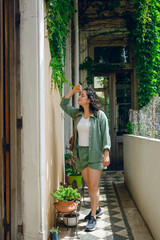 vertical image of young woman standing in entrance of her house caressing leaf of wall creeper plant