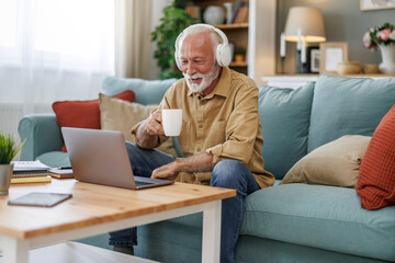 Senior man in casual clothing using laptop and smiling while working from home office