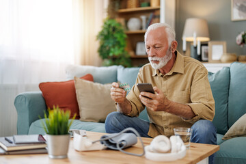 Senior man checking blood pressure at home - 706549982