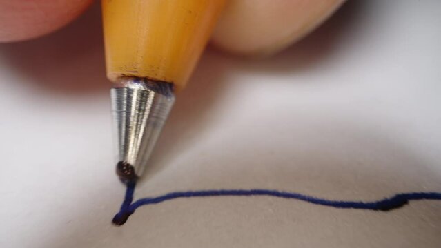 Ballpoint pen in hand, macro shot, ink flows through the ball at the end. It is writing something.