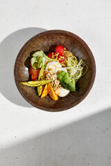 Top view of a salad bowl with avocado, mixed vegetables, and a poached egg in direct sunlight