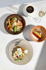 Overhead view of an eclectic breakfast with homemade yogurt, chicken and avocado bowl, crab with poached egg, coffee, and sparkling wine