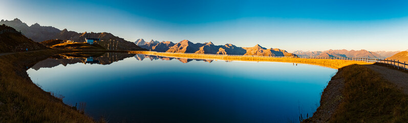 High resolution stitched alpine summer sunrise panorama with reflections in a lake at Mount...