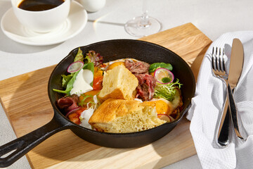 Sunny-side-up eggs in a skillet with roast beef, vegetables, and ciabatta, Americano coffee, and a glass of sparkling wine
