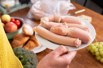 Hands holding a plate with boiled sausages.