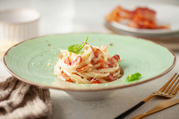 Spaghetti carbonara - pasta with bacon, creamy sauce and grated parmesan, garnished with basil leaf in  round ceramic plate. Italian cuisine