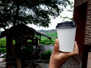 To-go drink. Woman holding paper cup of coffee on nature background.