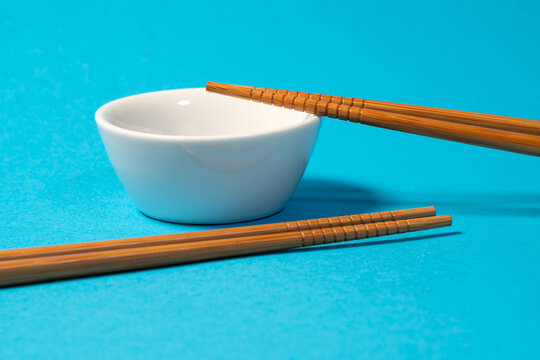 small white bowl with typical wooden chopsticks isolated on turquoise background