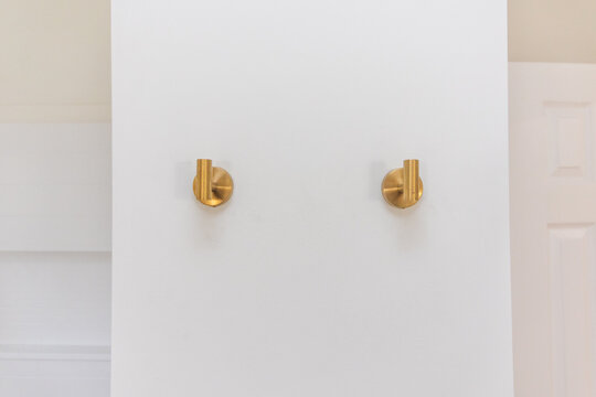 A set of two modern gold towel holder hooks or pegs on an empty blank wall in a bathroom in the interior of a home