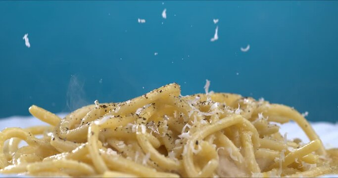 Super slow motion macro of professional chef is grating aged parmesan cheese on traditional Italian dish of pasta spaghetti with carbonara sauce isolated on soft background at 1000 fps.