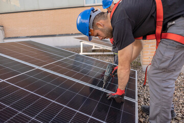Close up shot of worker installing a solar panel on a rooftop with his tool