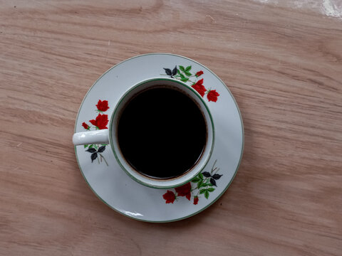 a cup of black coffee with a floral motif on the cup.