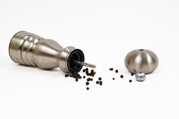 An open stainless steel pepper grinder with whole grain of pepper flowing out of it 