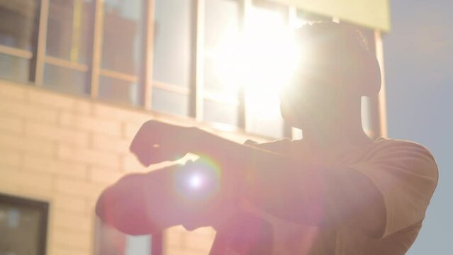 Happy dancing African American man male dancer having fun outdoors enjoy musical song listening to music earphones in city guy in headphones smiling laughing dance moving hands in sun lights sunbeams