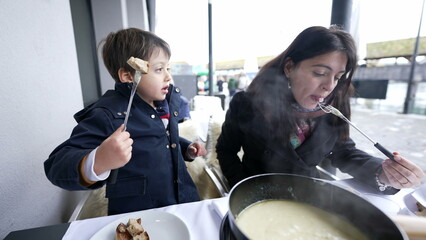 Mother and Child Relishing Swiss Fondue in December, Traditional European Cheese Cuisine at outdoor...