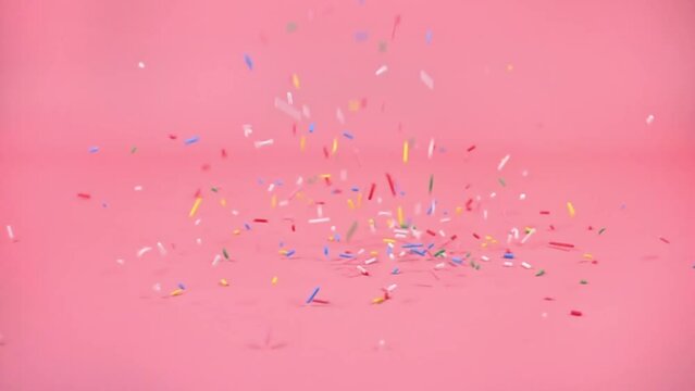 colorful sprinkles falling on pink background, decoration for cake and bakery, slow motion