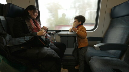 Mother and child traveling by train, little boy eating banana, mom giving son water to drink,...