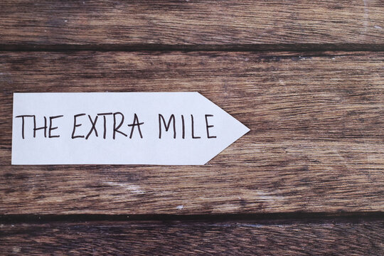 Extra mile handwritten text on paper arrow on wooden background. Top view. Copy space. Christian service, humility, and way of life, follow God Jesus Christ biblical concept.