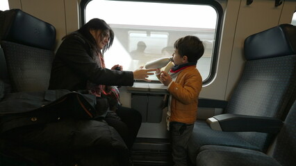 Mother and child traveling by train, little boy eating banana, mom giving son water to drink,...