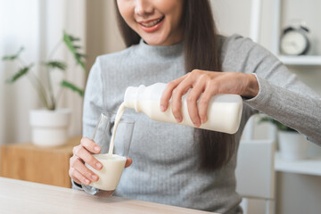 Health care, asian young woman, girl hand pouring of fresh, dairy milk from bottle into glass, drinking and eating breakfast in morning at kitchen home. Calcium, protein for healthy lifestyle people - obrazy, fototapety, plakaty