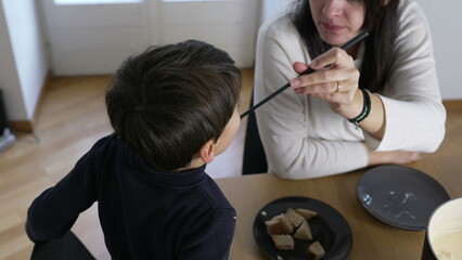 Mother and child eating fondue, mom feeding son traditional Swiss cuisine, European dish at home,...