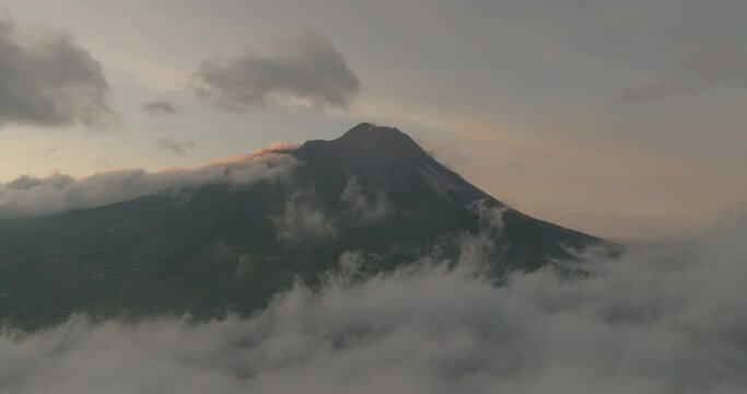 Aerial Idyllic View Of Active Volcanic Mountain Peak, Drone Flying Backwards Over Clouds During Sunset - Java, Indonesia
