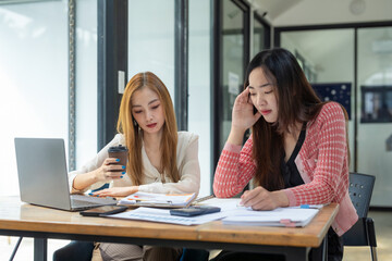 Two businesswomen sit with tense expressions looking at documents on a table in the office.