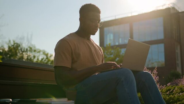 African American man student guy studying outdoors with computer male study in city near university college campus pensive looking away thinking homework task online learning with laptop in sunshine