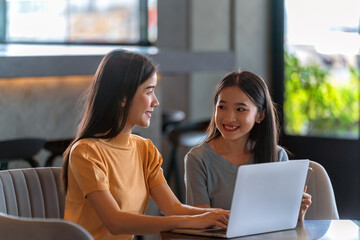 Fototapeta premium Weekend Out-of-Office Collaboration. Two young Asian woman break away from the office, opting for a cozy café to discuss work. 