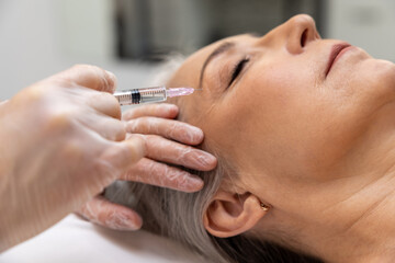 Beautician doing filler injections to a mature female patient