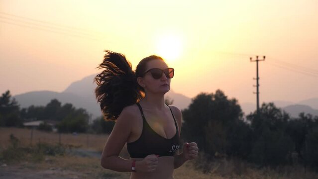 Sporty girl jogging in country road at sunset. Young woman running outdoors. Healthy active lifestyle. Slow motion Close up