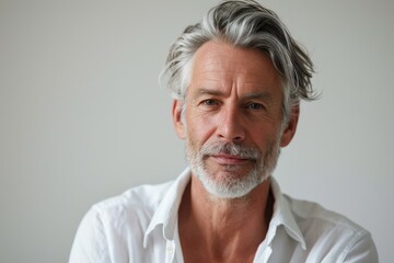 Portrait of a distinguished mature man with silver hair and a subtle, confident smile, wearing a crisp white shirt..