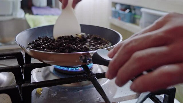 unrecognizable man stirring beans in a hot frying pan