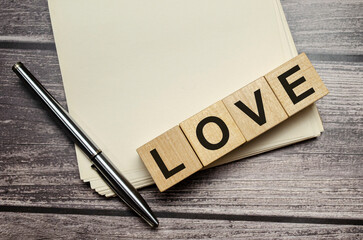 LOVE word on wooden block and pen with papers on wooden background - Powered by Adobe
