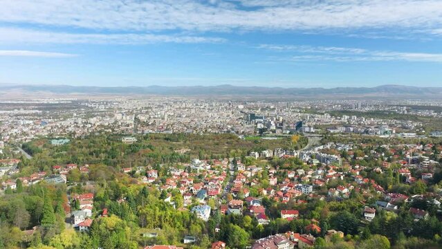 Aerial drone shot of Bulgarian capital Sofia, flying from outskirt Vitosha district towards city center on a sunny day with cirrus clouds.