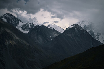 Altai’s snowy mountain ridge in dramatic light in summer, mountain silhouettes in gloomy weather,...