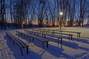 Ławki zimową porą w parku, śnieg i latarnie.