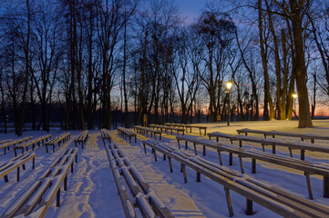 Ławki zimową porą w parku, śnieg i latarnie.