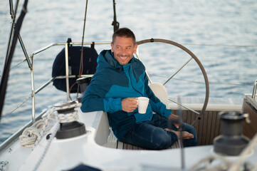 Man in blue jacket on the yacht having coffee and looking contented