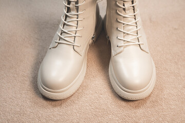 Beige winter women's leather boots on a beige background. Beautiful modern Shoes for bad weather wearing.