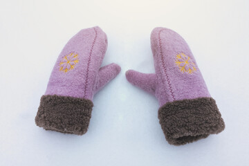 Cute pink winter women's mittens on the snow. Clothes for cold weather wearing.
