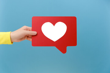 Close up of woman hand holding social media like stick, emoji notification button to follow and subscribe blog or post, popular forum, posing isolated over plain blue color background wall in studio